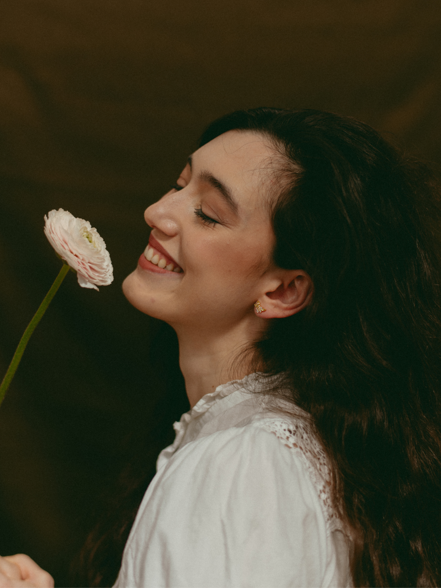 Woman holding a flower with flower stud earrings, white blouse, and long black hair