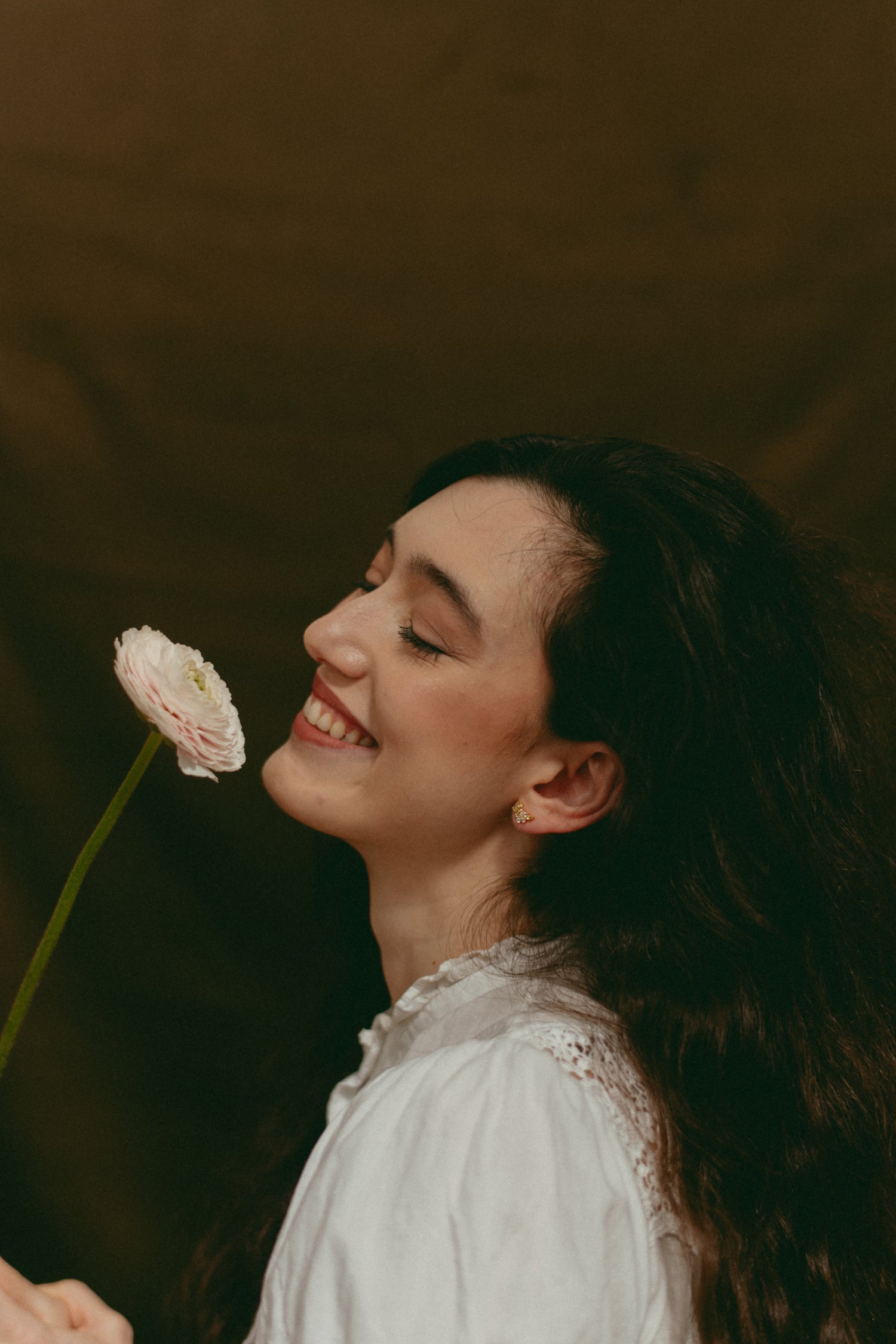 Woman holding a flower with flower stud earrings, white blouse, and long black hair