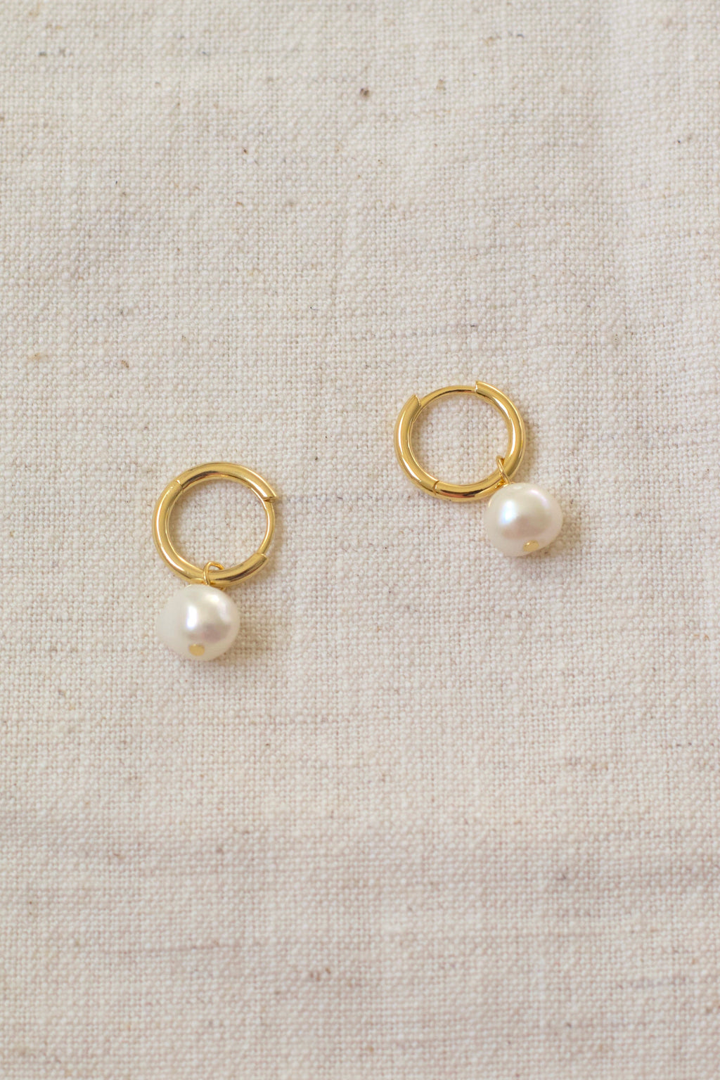Gold hoop earrings with pearls on a beige fabric background