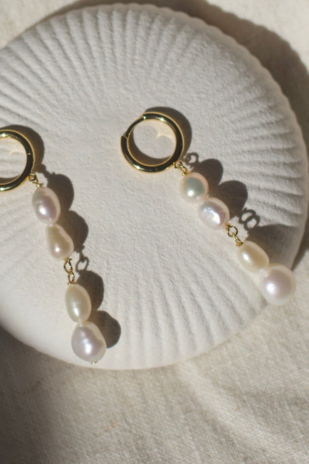 Pearl earrings on a white shell against a textured beige background
