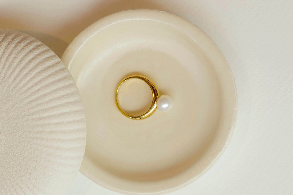 Gold ring with a pearl on a beige shell-shaped jewelry box