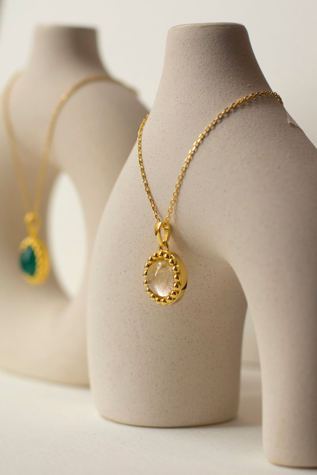 Two gold necklaces in green onyx and yellow rutilated quartz on ceramic sculptures