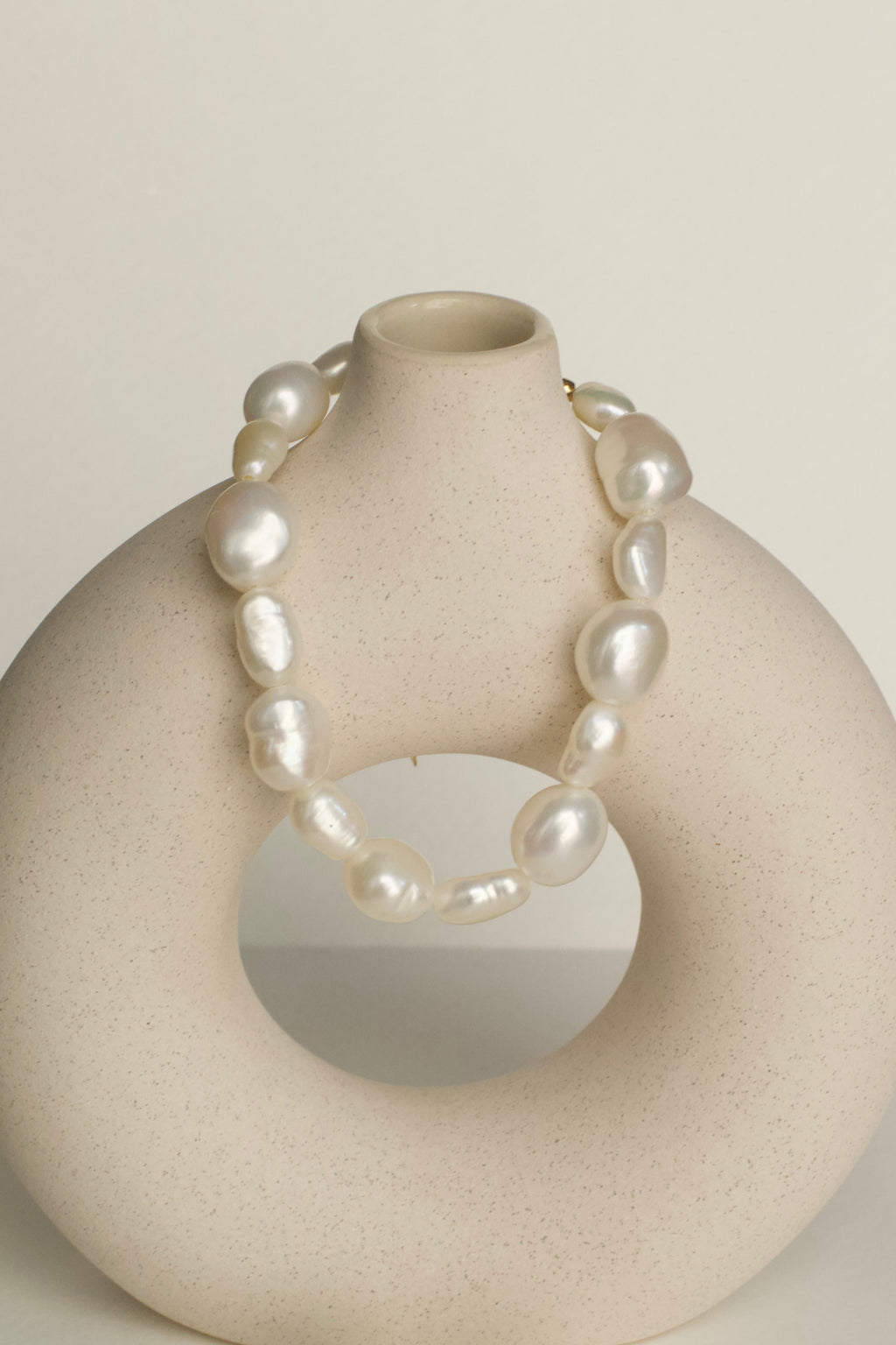 Natural pearl bracelet on a beige vase against a plain background