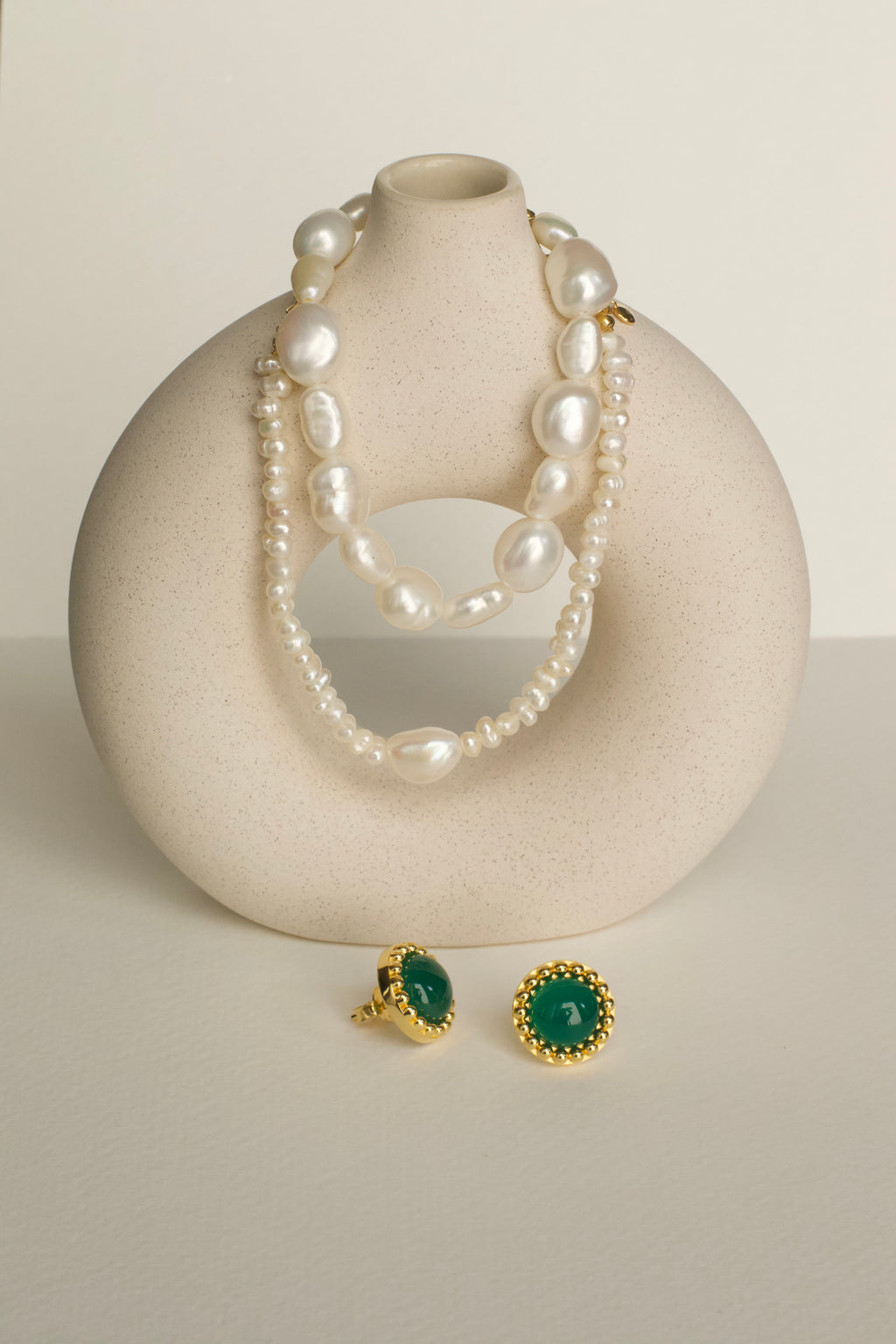 Pearl necklace and green gemstone earrings on a white surface with a neutral background