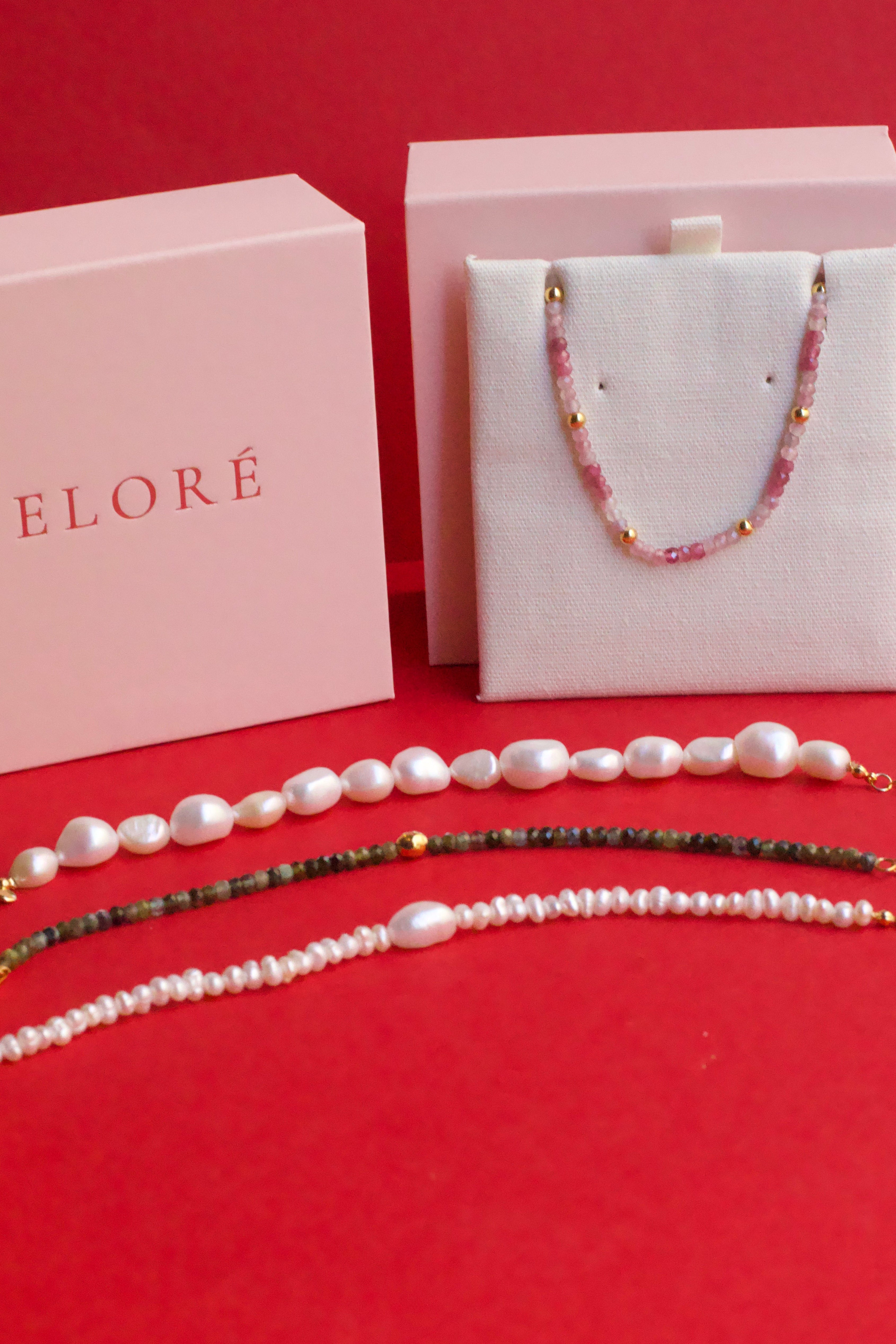 Pearl and tourmaline bracelets on a red surface with 'ELORE' branding.