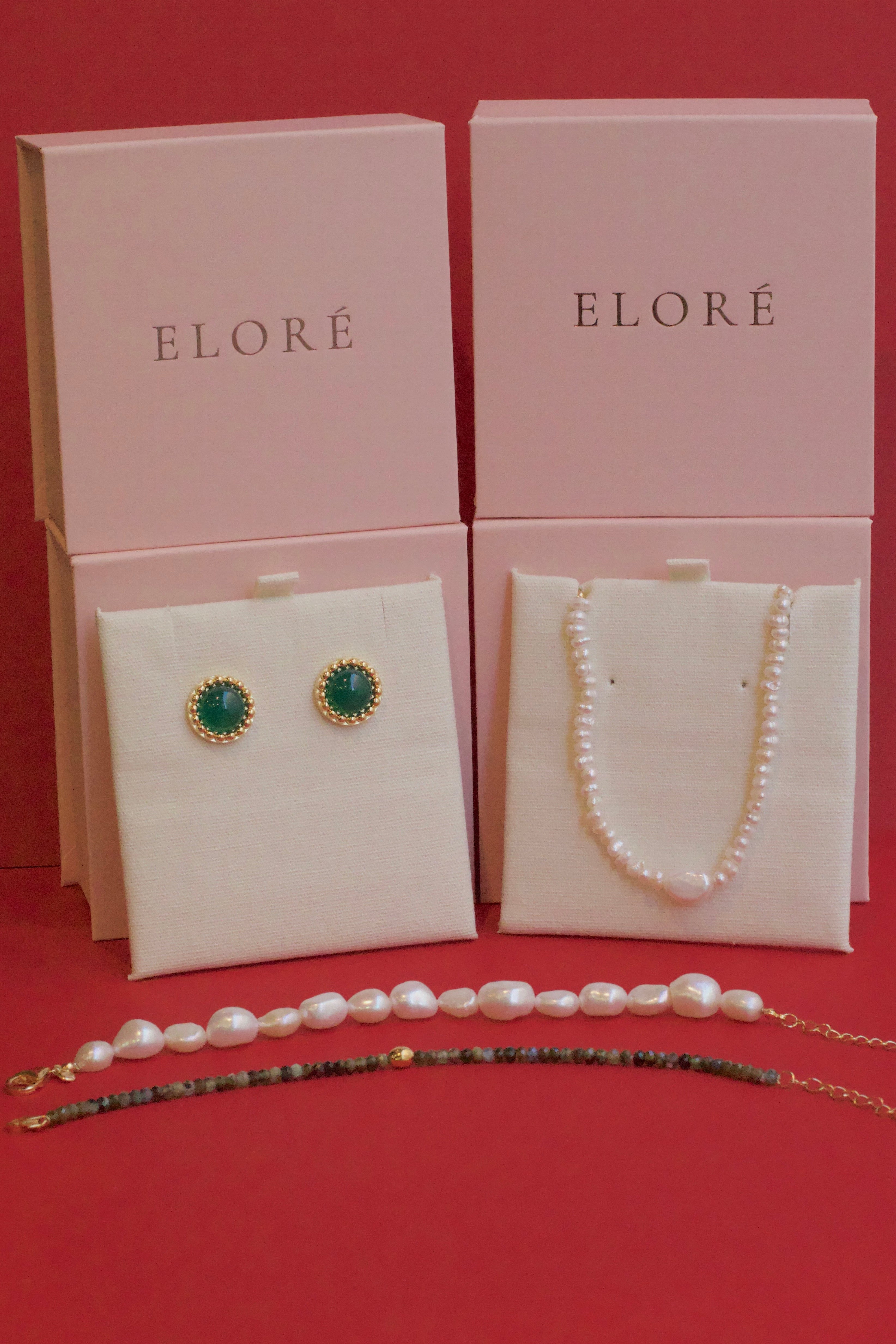 Earrings, necklace, and bracelet with 'ELORE' packaging on a red background.