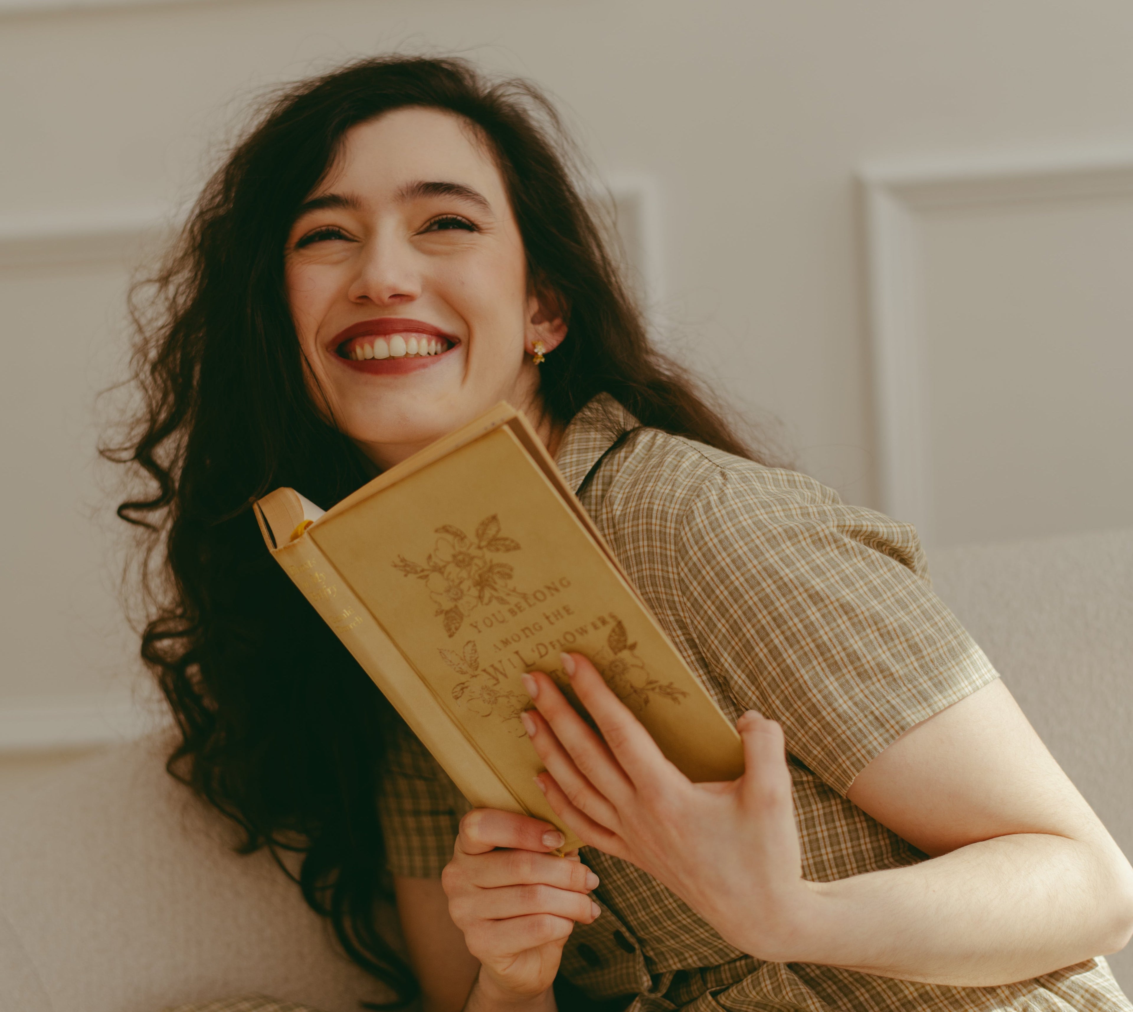 Woman holding a yellow book and smiling in a room with white walls.