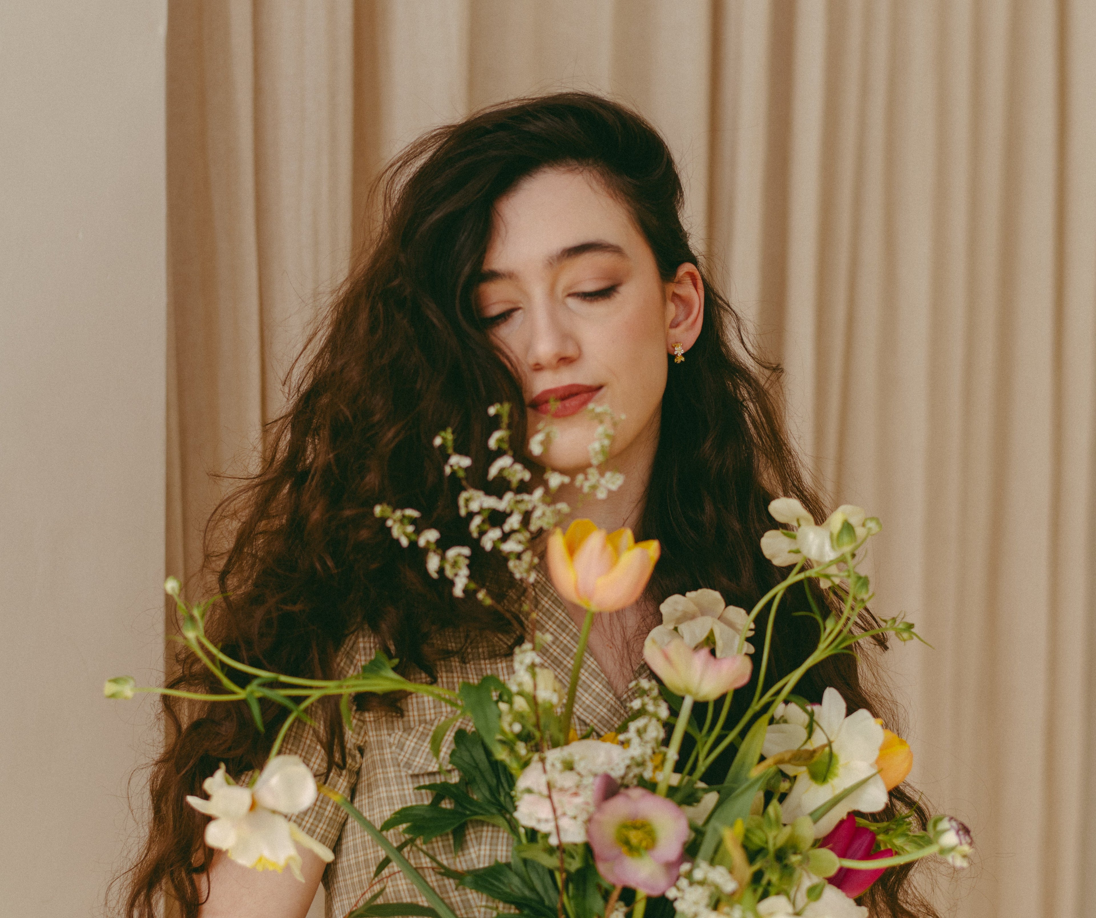 Woman holding a bouquet of flowers against a beige curtain background